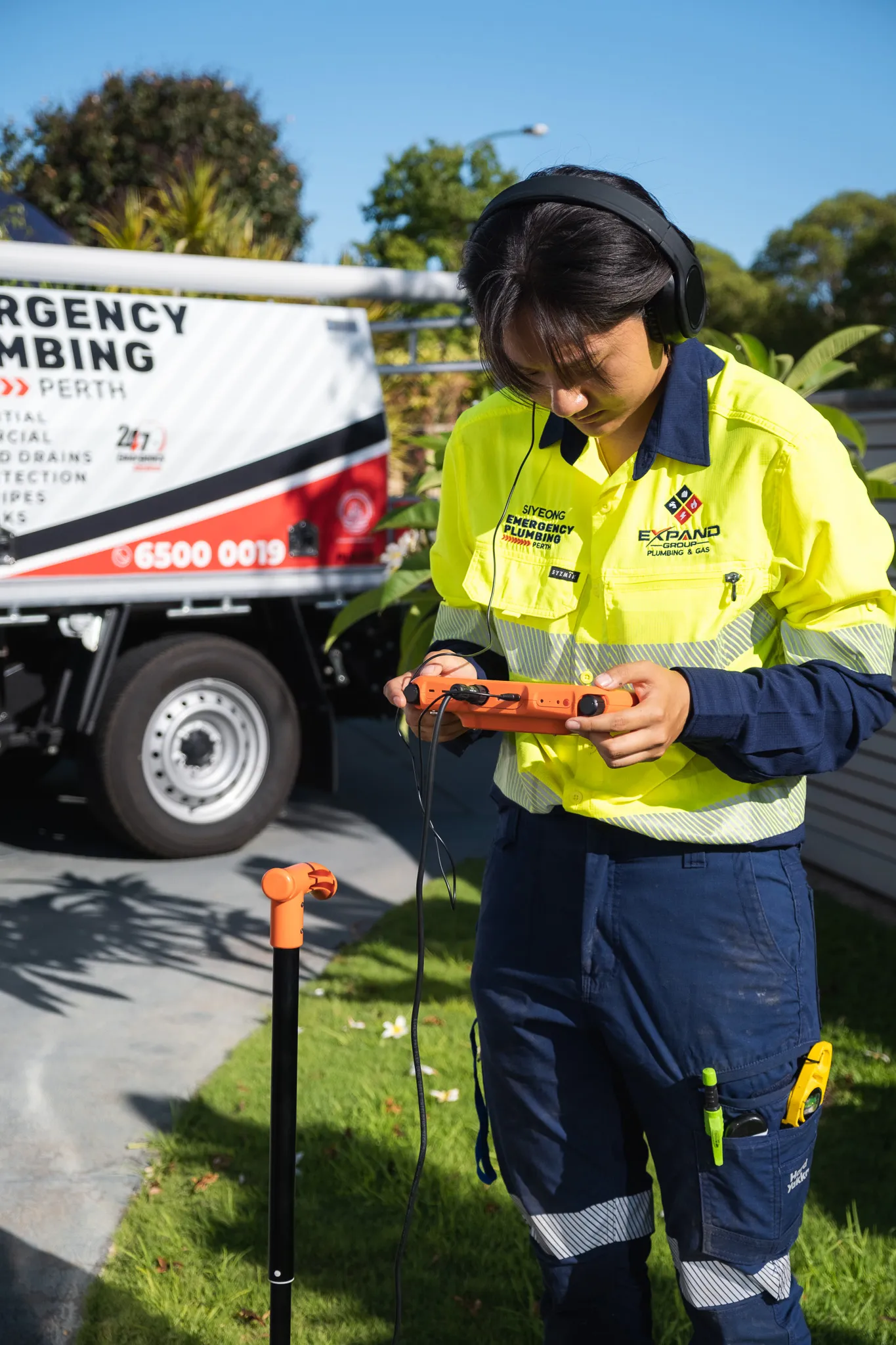 Licensed plumber in a high-visibility uniform using a leak detection device near a service vehicle in Perth