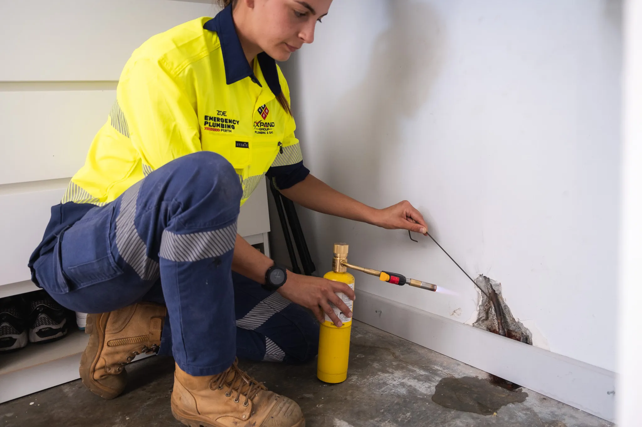 A technician in a yellow shirt using a torch near a wall for repair