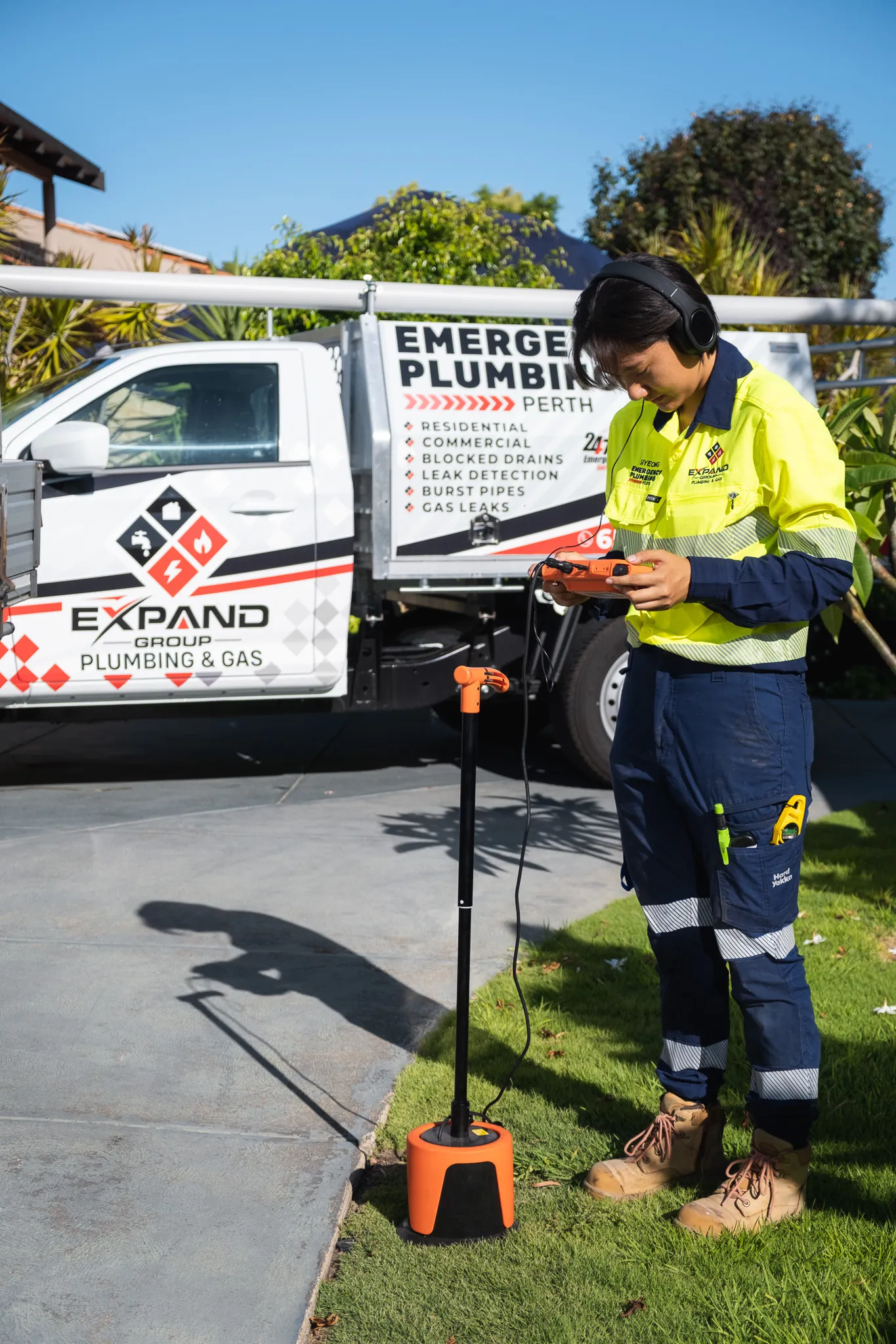 Technician using a gas leak detection device near a plumbing service truck.