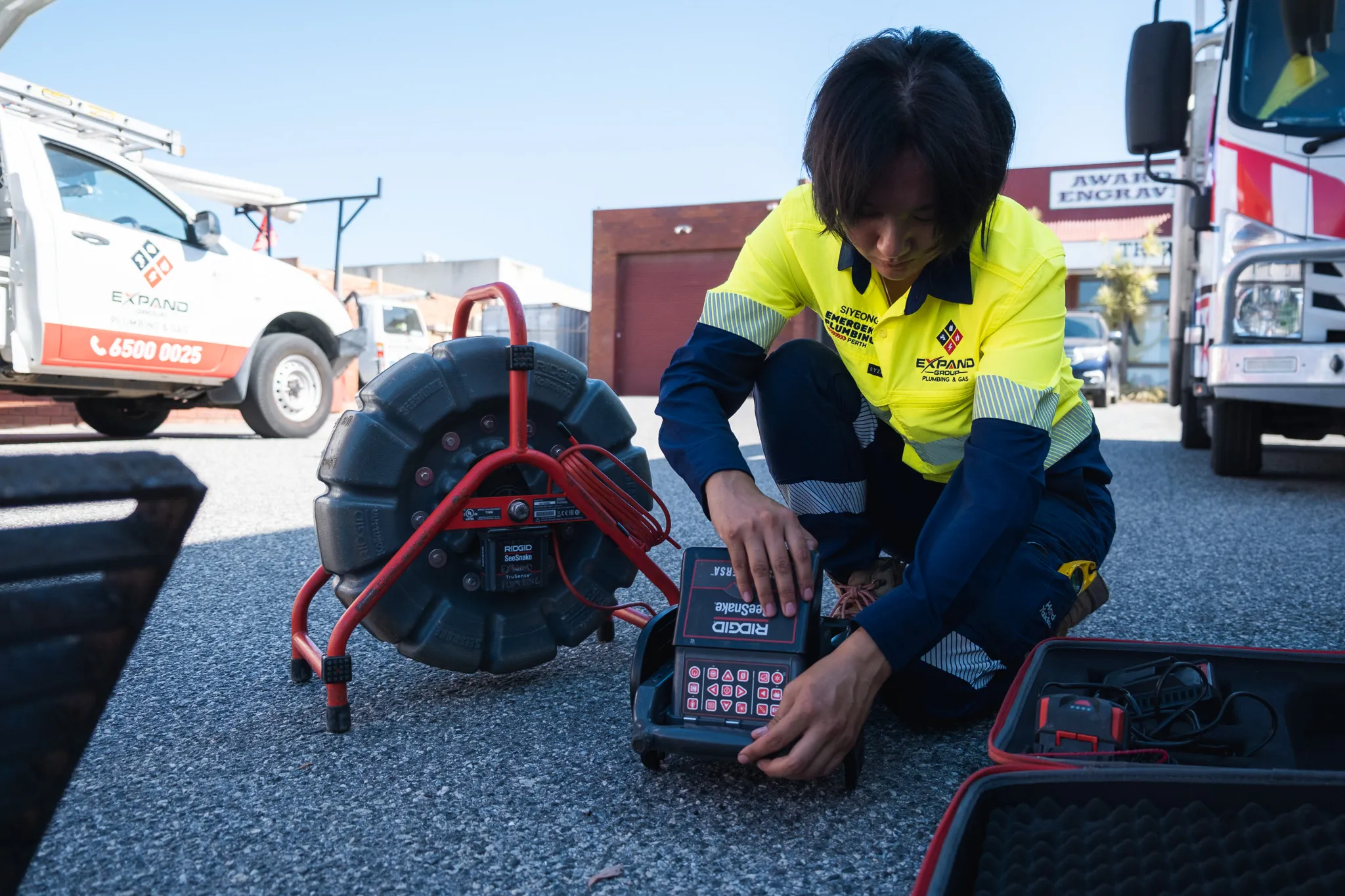 Technician using equipment to inspect pipes, with a cable reel nearby.